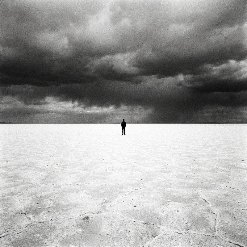 Vast salt flat, lone figure silhouette against stormy sky